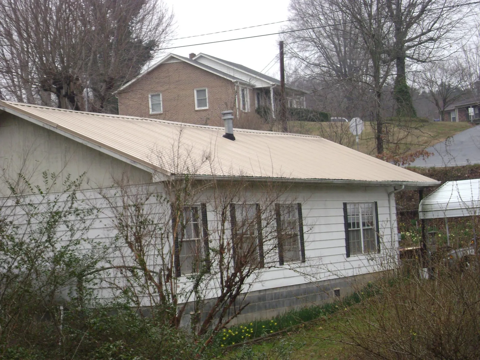 Tan metal roof on a white sided house set into a hillside — Commercial Roofing by Roofing Brothers in Sherwood